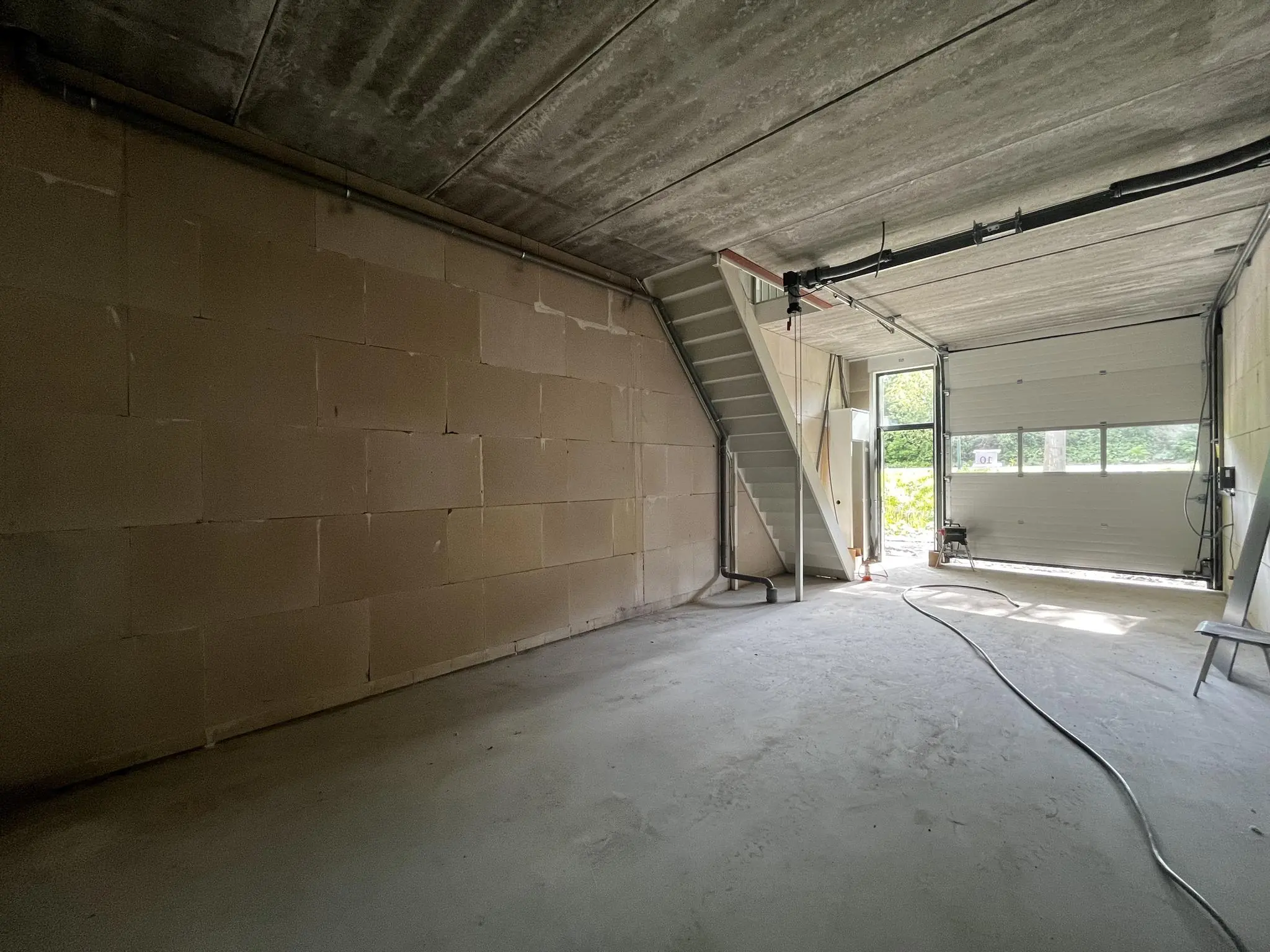 Lege garage- of bedrijfsruimte aan de Broekdijk West met betonnen vloer, trap naar boven en openstaande roldeur.